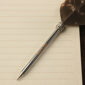 Op de afbeelding: Een zilveren pen met een veerpenpunt en een decoratieve zilveren dop. De pen heeft het woord "DAVID" gegraveerd op de huls.