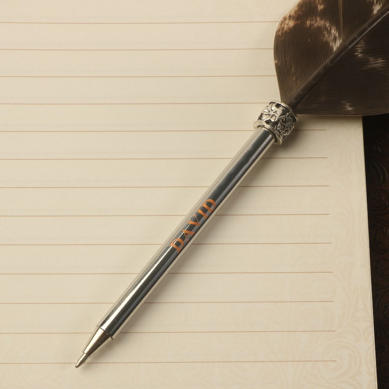 Op de afbeelding: Een zilveren pen met een veerpenpunt en een decoratieve zilveren dop. De pen heeft het woord "DAVID" gegraveerd op de huls.