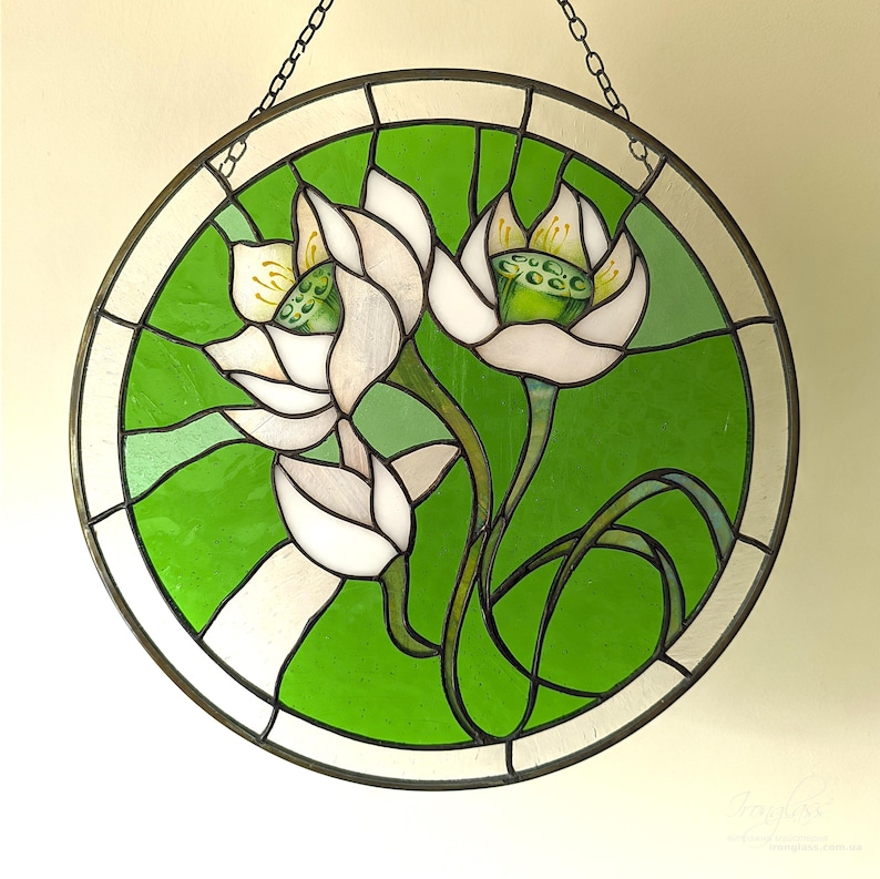 Elegant round stained glass panel featuring White lilies and a variegated green background, centered against a light wall, highlighting the detailed flower suncatcher design and the quality of the glasswork.