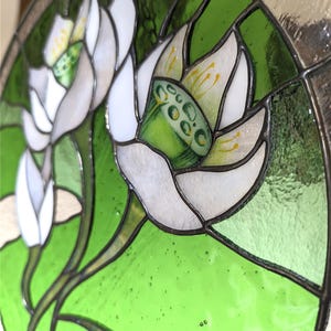 Tilted close-up of the stained glass panel, focusing on one White lilies flower bloom, showing the vibrant green seed pod and yellow hand-painted details, emphasizing the high-quality tiffany glass art.