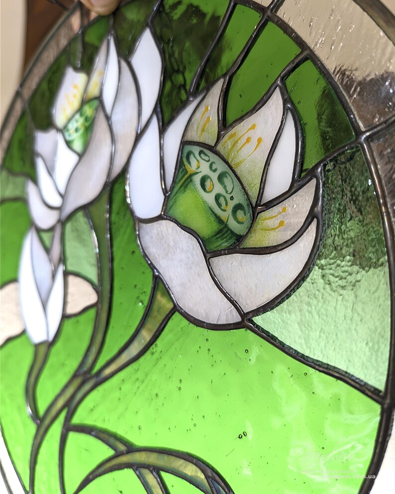 Tilted close-up of the stained glass panel, focusing on one White lilies flower bloom, showing the vibrant green seed pod and yellow hand-painted details, emphasizing the high-quality tiffany glass art.