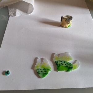 In-progress shot showing the hand-painted high-quality American glass pieces used for the lily stamens and seed pods on a white background, highlighting the authentic tiffany glass art technique.