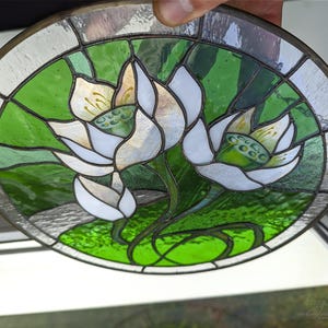 Hand-held close-up of the round stained glass panel, clearly showing the craftsmanship of the Tiffany glass art technique and the included natural eco-linen thread for easy display as a windows hangings.