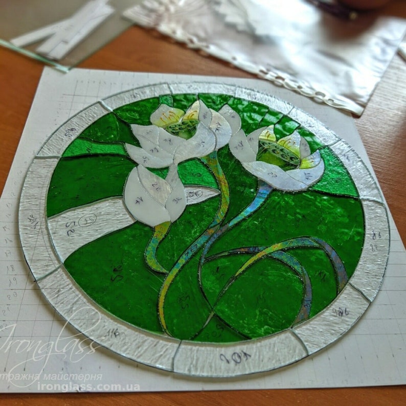Overhead view of the stained glass panel in an intermediate stage of creation, showing the precisely cut and ground American glass pieces of White Lilies arranged on the design pattern before soldering, highlighting the detailed tiffany glass art craftsmanship.