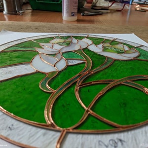 Overhead studio shot showing the Tiffany glass art process, with all cut and ground glass pieces wrapped in copper foil and arranged on the pattern, illustrating the preparation stage before soldering the stained glass panel.
