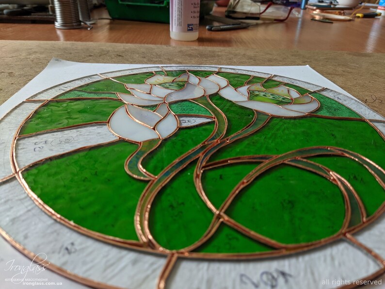 Overhead studio shot showing the Tiffany glass art process, with all cut and ground glass pieces wrapped in copper foil and arranged on the pattern, illustrating the preparation stage before soldering the stained glass panel.
