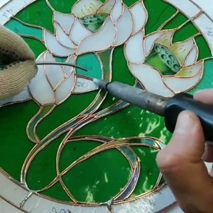 Soldering a stained glass window with lilies using tin solder, the hands of a master