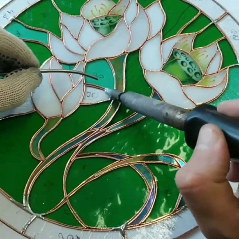 Soldering a stained glass window with lilies using tin solder, the hands of a master