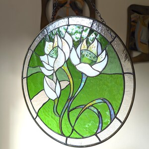 Round window wall hanging featuring White lilies, showcasing the glossy edge glass and the bright green background as a stunning flower suncatcher piece of decor in a contemporary interior setting.
