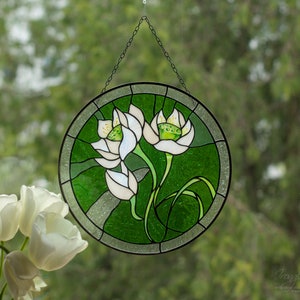 The round white lilies flower windows hangings displayed on a windowpane, contrasted against fresh green garden flower decor and a bouquet of real white tulips, emphasizing its use as a beautiful flower suncatcher.