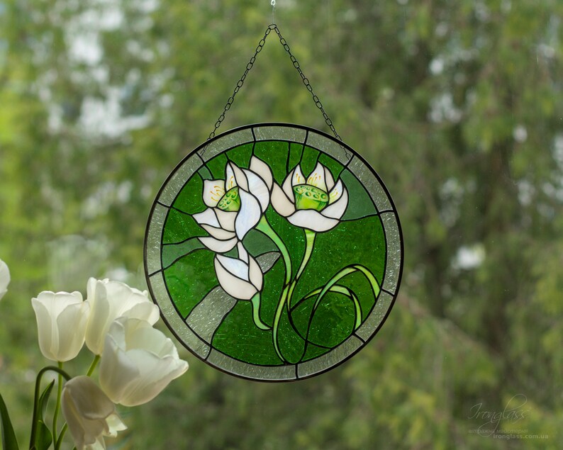 The round white lilies flower windows hangings displayed on a windowpane, contrasted against fresh green garden flower decor and a bouquet of real white tulips, emphasizing its use as a beautiful flower suncatcher.