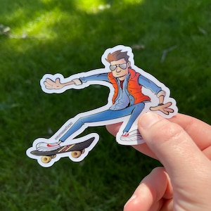 Puede incluir: Una pegatina de dibujos animados de una persona que lleva un chaleco rojo y pantalones vaqueros azules, haciendo skateboard. La pegatina tiene el texto "@HOFFMANTOONS" en la tabla de skate.