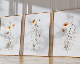 May include: Three framed watercolor paintings of wildflowers in shades of orange, yellow, and brown. The paintings are set against a white background and are framed in gold.