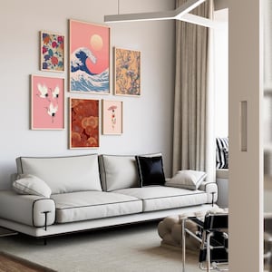May include: A modern living room featuring a white sofa with black trim, a collection of framed art prints, and a neutral color palette. The art includes a wave, cranes, and floral designs. A black pillow and a light gray rug complete the scene.