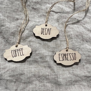 May include: Three wooden tags with twine attached, each with a different coffee type written on them: "Decaf", "Coffee", and "Espresso".