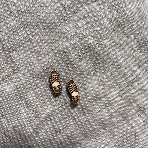 May include: Two small wooden shoe prints, one brown and one black, on a light gray fabric background.
