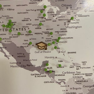 May include: A world map with green push pins marking locations across North America, Central America, South America, and the Caribbean. A graduation cap is placed on the map over the Gulf of Mexico.
