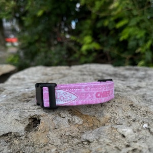 Puede incluir: Collar de perro rosa con hebilla negra y logotipo blanco de los Kansas City Chiefs. El collar tiene un dise&ntilde;o estampado rosa y blanco.