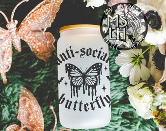 May include: White frosted glass jar with a black butterfly graphic and the text "anti-social butterfly". The jar is sitting on a green surface with two gold glitter butterflies.
