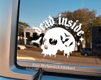 May include: White vinyl decal on a car window featuring a skull with bats and the words "dead inside." The decal has a gothic font and a spooky theme. The Etsy shop name "MySpookyLittleHeart" is also visible.