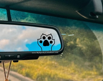 May include: A rearview mirror in a car with a paw print sticker and the text "www.MyspookyLittleHeart.com". A car air freshener hangs from the mirror.