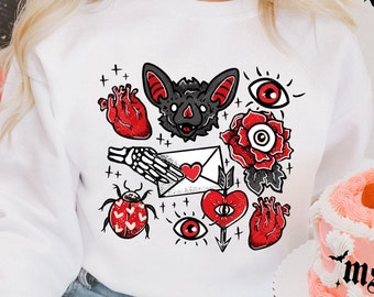 May include: White sweatshirt with a graphic print of a bat, hearts, eyes, a rose, a ladybug, and a skeleton hand holding a letter. The graphic is in black and red.