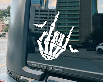 May include: A black car with a white skeleton hand giving the middle finger with bats flying around it. The car has a sticker that says "www.MySpookyLittleHeart.com".