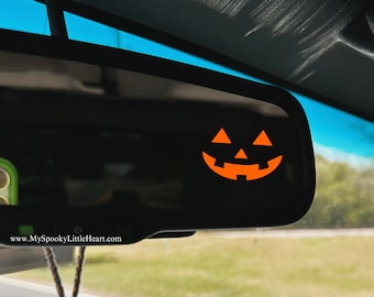 May include: A rearview mirror with a pumpkin face sticker. A skull-shaped car air freshener hangs from the mirror. The website www.MySpookyLittleHeart.com is visible on the mirror.