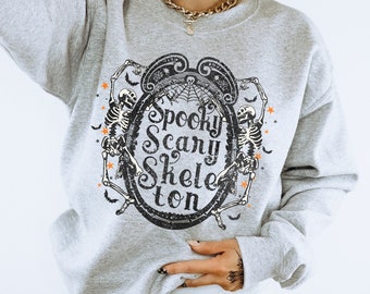 May include: Gray sweatshirt with a spooky skeleton graphic and the text "Spooky Scary Skeleton" in a vintage font. The sweatshirt is worn by a person with a gold chain necklace.