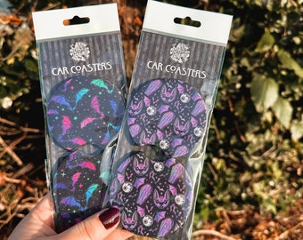 May include: Two sets of car coasters featuring a black background with a repeating pattern of bats, eyes, and coffins. The coasters are packaged in clear plastic bags with the text "CAR COASTERS" printed on the front.