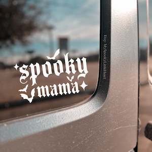 May include: White vinyl decal with the text "spooky mama" in a gothic font. The decal has several small bat silhouettes around the text.