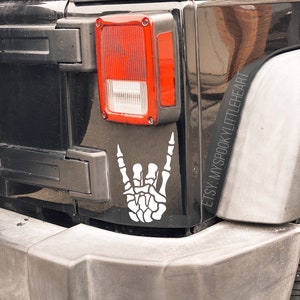 May include: A black Jeep with a white skeleton hand making the rock and roll sign. The sticker says "Etsy: MySpookyLittleHeart".