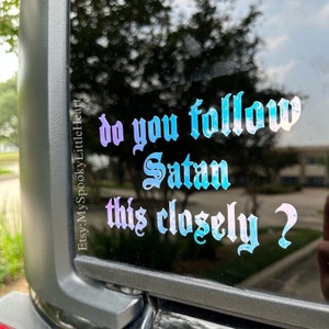 May include: A sticker on a car window with a gradient of blue and purple. The sticker says "Do you follow Satan this closely?" in a gothic font.