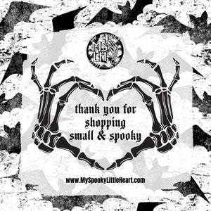Pu&ograve; includere: Immagine in bianco e nero di due mani scheletriche che formano un cuore. Le mani sono circondate da pipistrelli e dal testo "thank you for shopping small & spooky" e "www.MySpookyLittleHeart.com".