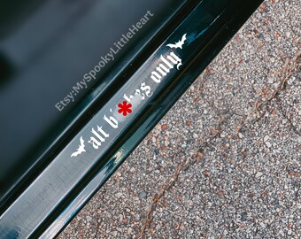 May include: A white vinyl decal applied to a dark surface, featuring the text "alt b*t*hes only" in a gothic-style font. The design is flanked by two small white bat silhouettes, one on each end of the text, with a red asterisk replacing the letter i.