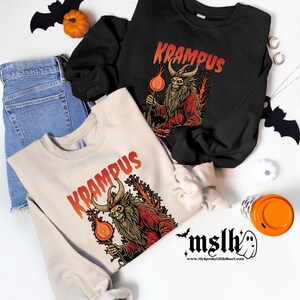 May include: Two cream and black long-sleeved sweatshirts with a graphic print of a red and black creature with horns and a beard. The text "Krampus" is printed in red on both sweatshirts.