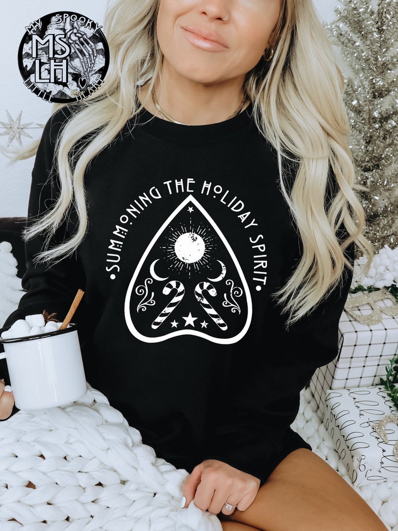 May include: Black sweatshirt with a white graphic of a Ouija board with candy canes and the text "Summoning the Holiday Spirit."