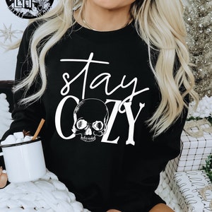 May include: Black sweatshirt with white text that reads "stay cozy" and a skull graphic.