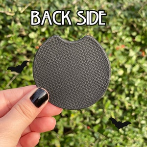 May include: Black round coaster with a textured surface. The coaster has a slightly curved edge. The text "BACK SIDE" is visible in the background.