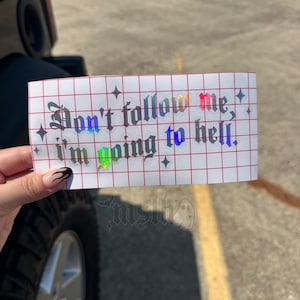 May include: A rectangular adhesive decal featuring the text "Don't follow me, i'm going to hell." in a gothic font. The lettering has a holographic finish that reflects various colors. The decal is applied to a white backing with a red grid pattern.