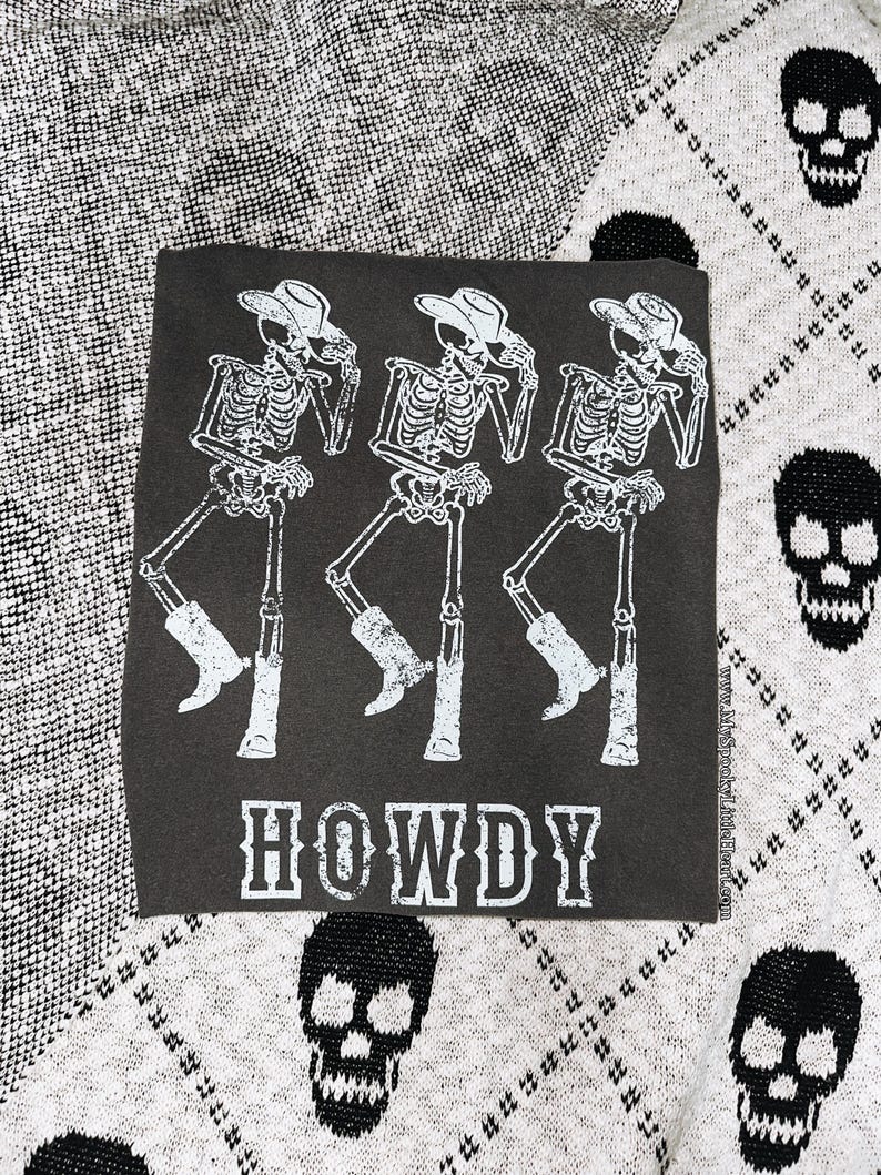 May include: Dark gray square with a white graphic of three skeleton cowboys wearing hats and boots, with the word "HOWDY" in bold white letters. The background is a gray and white skull pattern.