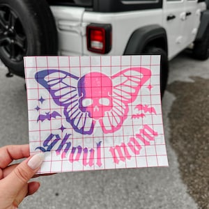 May include: A pink and purple vinyl sticker featuring a skull and butterfly design with the text "Soul Mates". The sticker has a grid backing and is held up in front of a white Jeep.