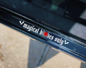 May include: A white vinyl decal applied to a black surface featuring the text "magical b*tches only" in a gothic font. The letter "i" in the word "b*tches" is replaced by a red asterisk, and small white bat silhouettes flank the text.