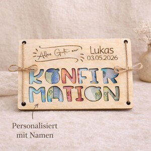 May include: A wooden plaque with the word "KONFIRMATION" cut out, revealing colorful money inside. The plaque has the name "Lukas" and the date "03.05.2026" engraved. It is tied with twine and has the text "Personalisiert mit Namen".