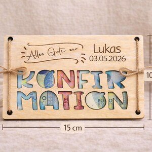 May include: A wooden plaque with the word "KONFIRMATION" cut out, filled with colorful currency. The plaque is 15 cm wide and 10 cm tall, with the text "Alles Gute zur Lukas 03.05.2026" engraved on top. Twine is used for hanging.