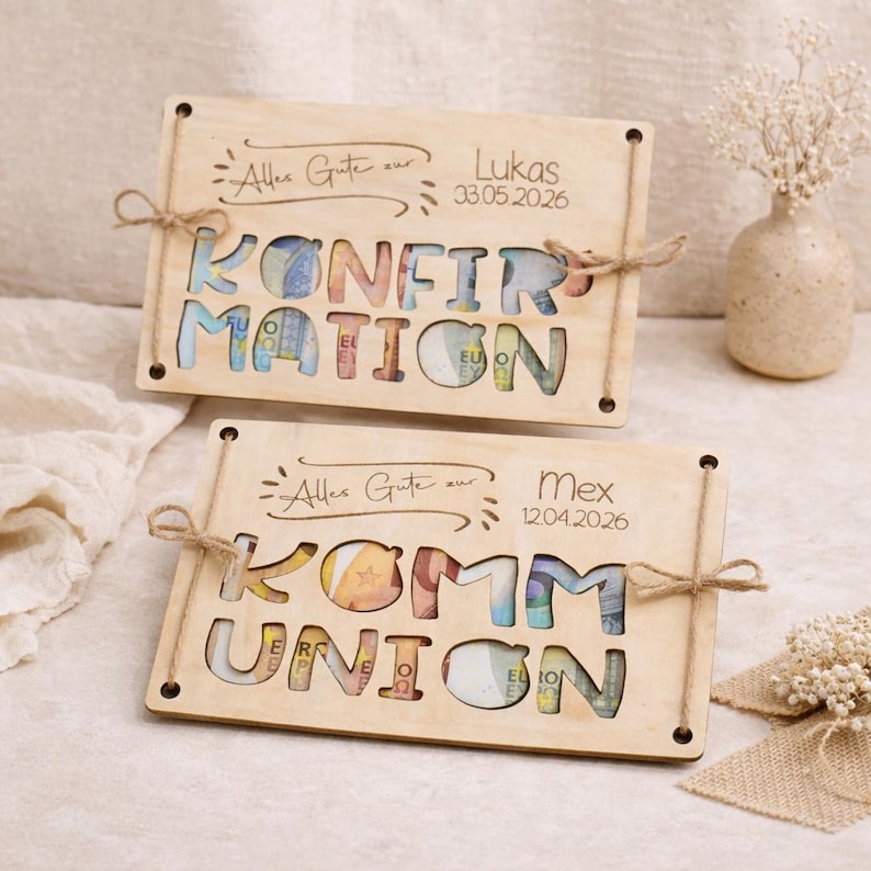 May include: Two wooden plaques with cut-out letters spelling "KONFIRMATION" and "KOMMUNION", filled with Euro banknotes. Each plaque has a name and date, tied with twine. The background includes a vase with flowers.