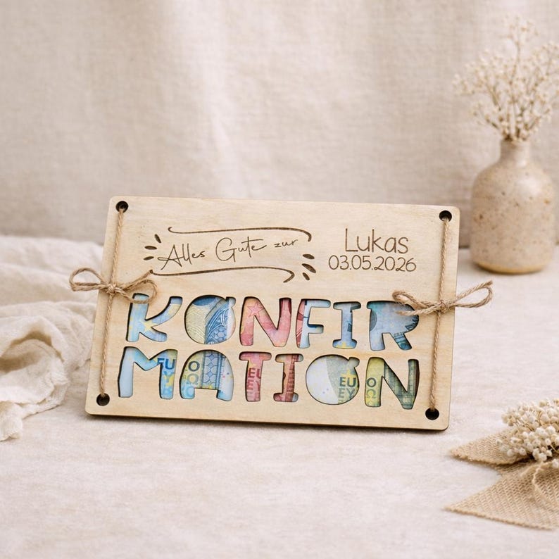 May include: Wooden plaque with the word "KONFIRMATION" cut out, filled with colorful currency. The plaque has the text "Alles Gute zur Lukas 03.05.2026" and is tied with twine. A decorative gift for a confirmation.