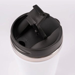 May include: A white travel mug with a black lid and a flip-top lid. The lid has a rubber seal to prevent spills.