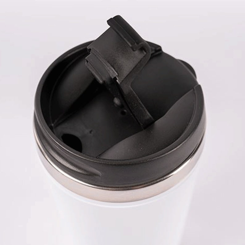 May include: A white travel mug with a black lid and a flip-top lid. The lid has a rubber seal to prevent spills.