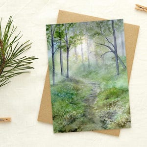 May include: Watercolor art print of a forest scene with a path leading through the trees. The artwork features a palette of greens and blues, with a soft, misty atmosphere. The print is on a white background with a brown card.